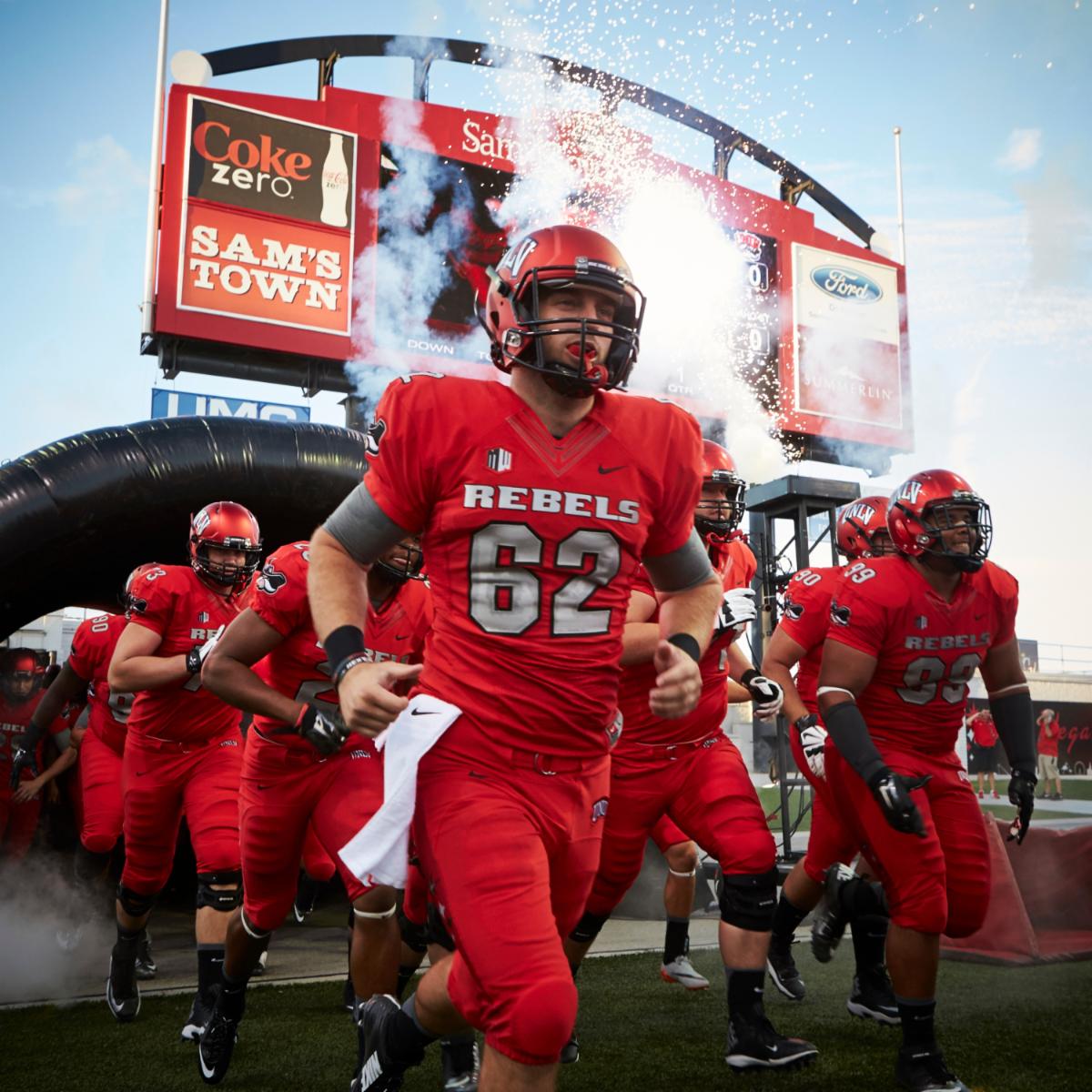 Football players in Rebel red run onto the field at Sam Boyd Stadium