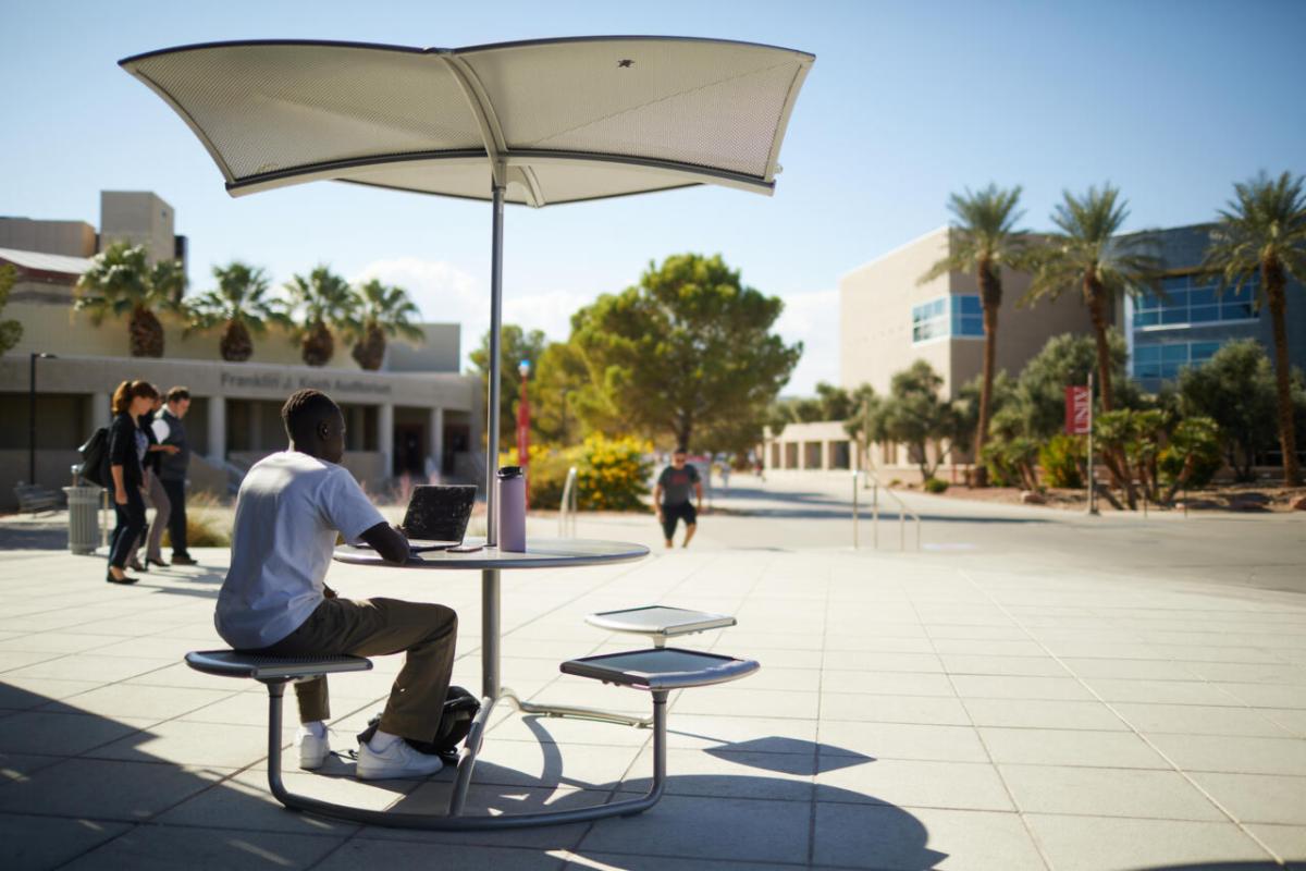 Person sitting at an outdoor table under an umbrella in the sun