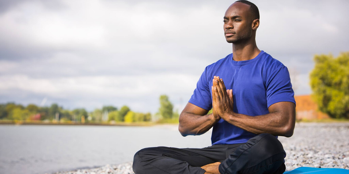 This is a photo of a dark skinned Black man wearing a blue shirt and black pants doing yoga 
