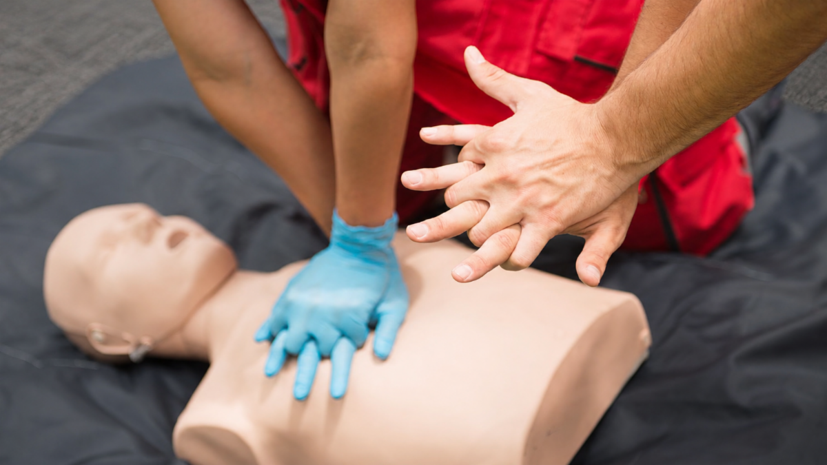 A person performing CPR on a dummy while receiving instruction