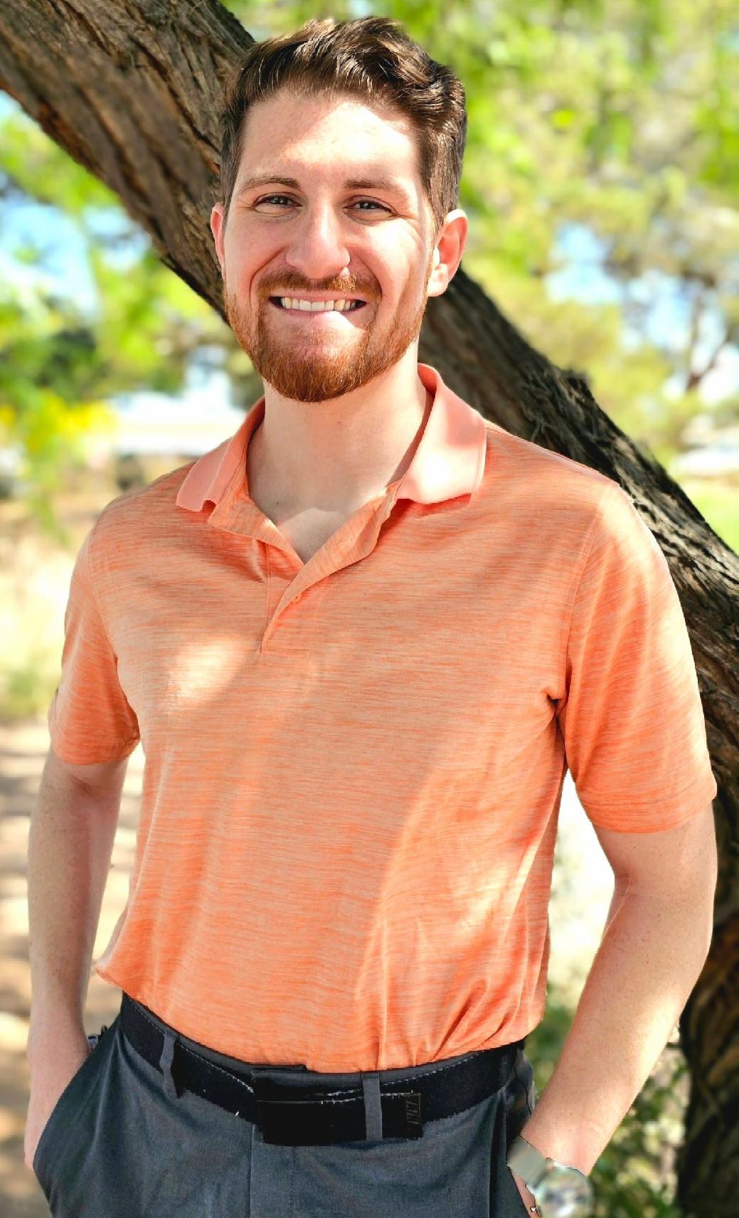 A white man with red hair dressed in an light orange shirt and gray pants