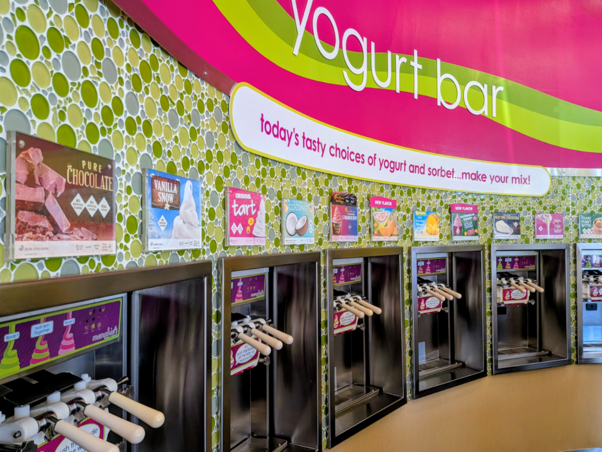 Menchie's Frozen Yogurt dispensing handles with flavor posters. Sign says "Yogurt Bar" with subtitle "Today's tasty choices of yogurt and sorbet... make your mix!"