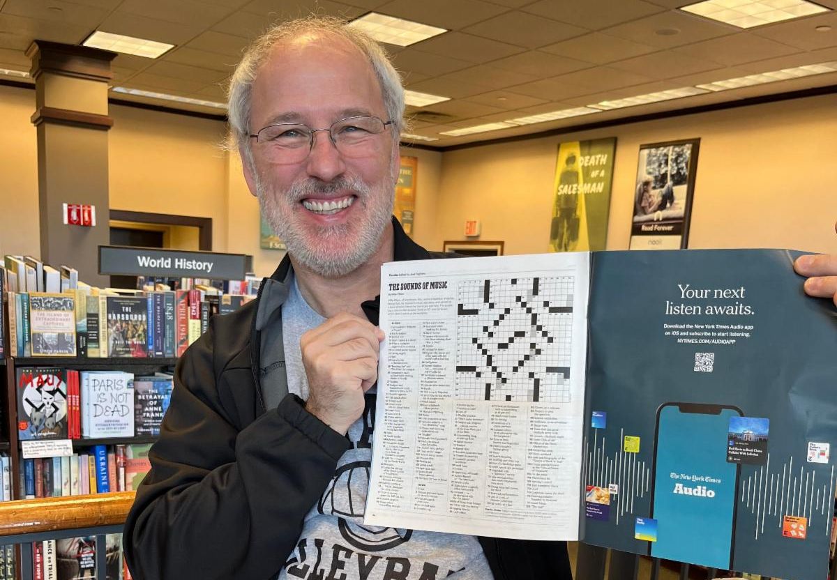 Mike Ellison, a white man with a beard, holding up a crossword puzzle