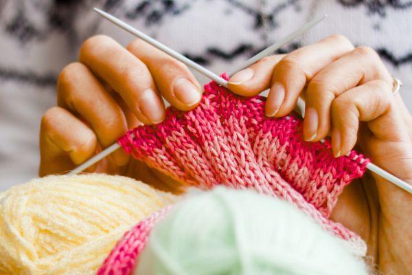 Pair of hands knitting a pink scarf
