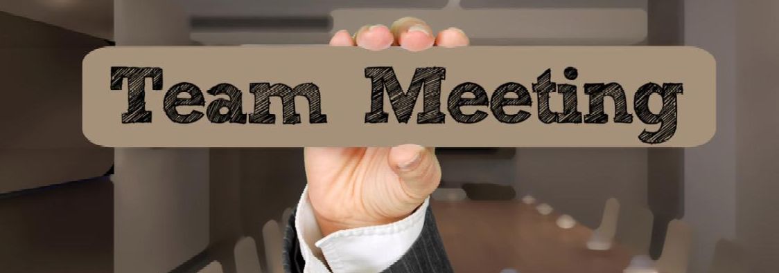 The hand of a white man holding a placard that says Team Meeting