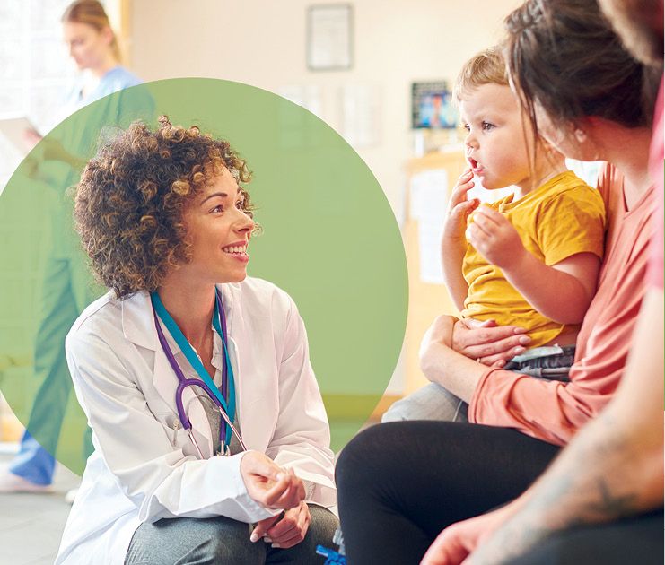 Female provider, kneeling next to parents holding small child.
