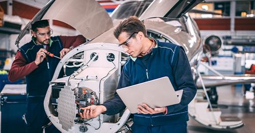 mechanics using a laptop and hand tools to work on aircraft