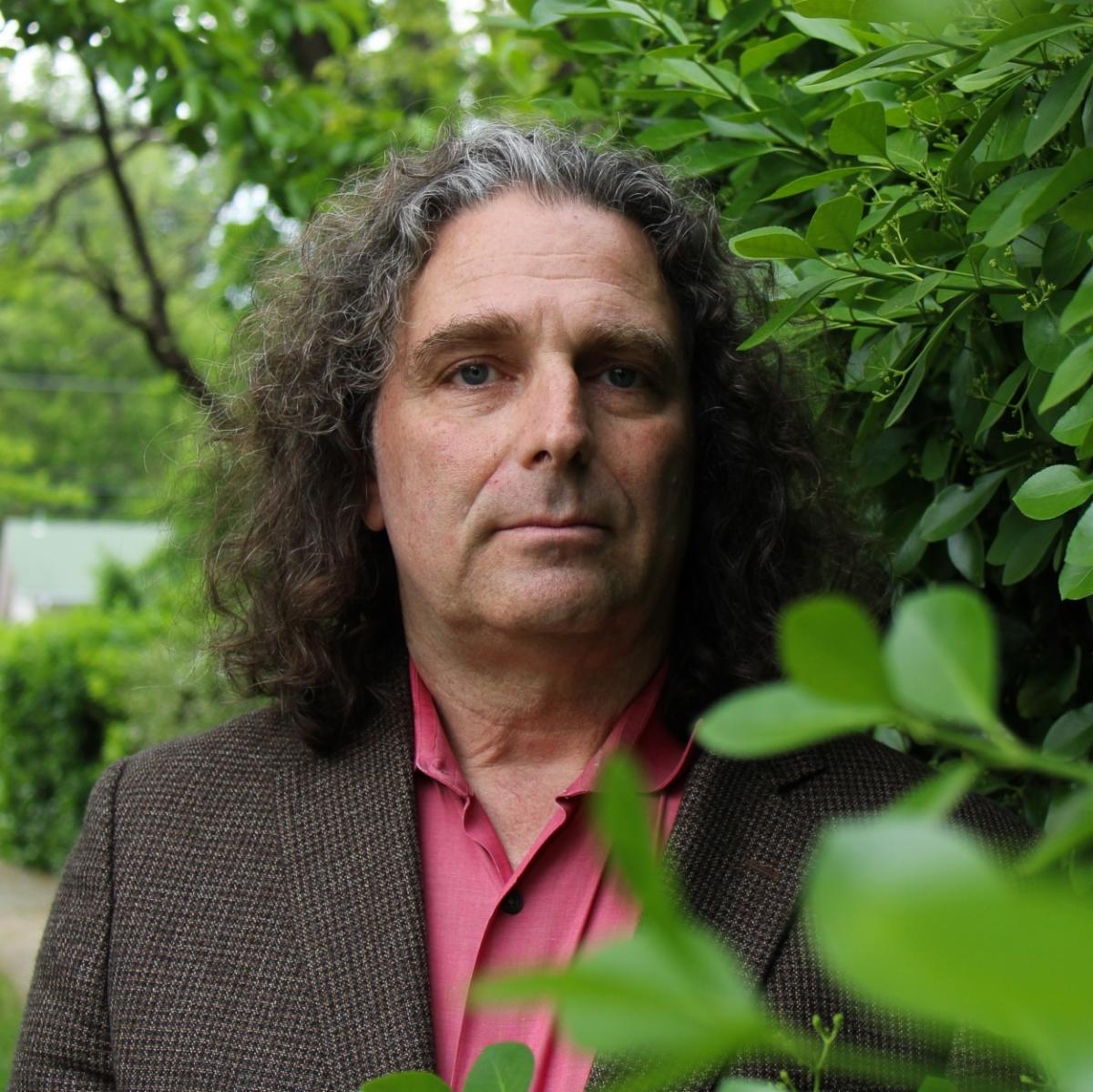 Philip Resnik stands against a green leafy bush