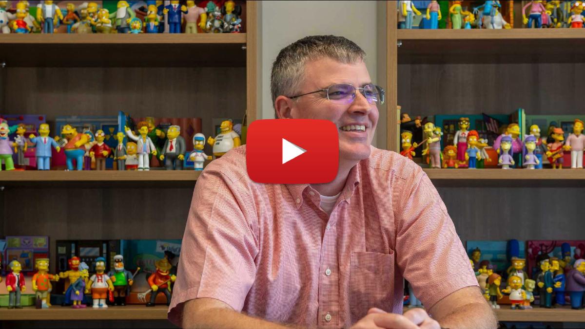YouTube screenshot of Derek Yarnell with a collection of "The Simpsons" figurines behind him on bookshelves 