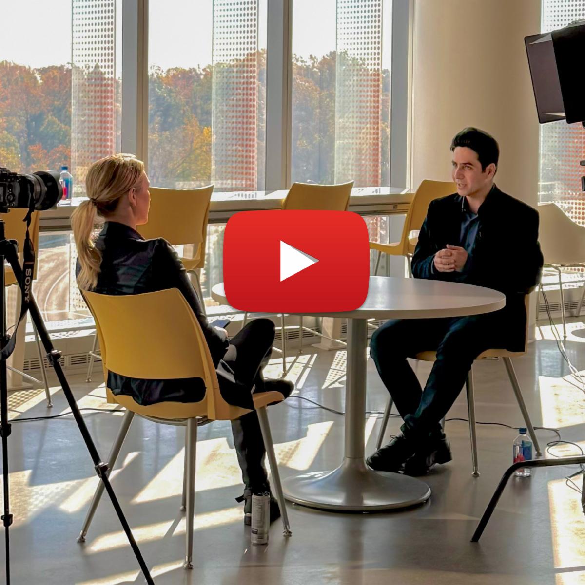 Soheil and blond woman reporter sitting down at table for interview