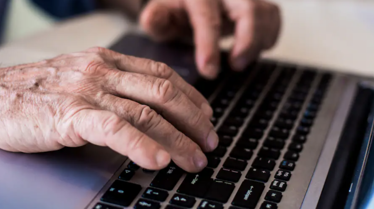 Photo shows hands of older adult typing on a computer keyboard