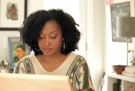 A black woman with short curly dark hair concentrates at a drawing table