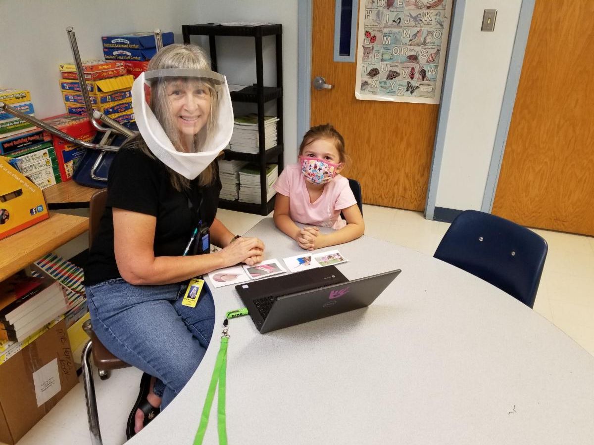 Photo of Dawnie Clark sitting with a student at a table working on Fingerspelling Our Way to Reading curriculum. Both Dawnie and the student are wearing face coverings.