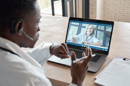 Black man sitting in front of his laptop and speaking during a virtual meeting with a white woman.