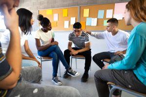 Group of teens sitting in a circle in a support group setting looking at one distressed teen.