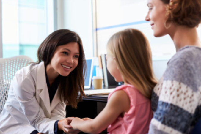 A doctor talks to a young patient and her mom in her office.