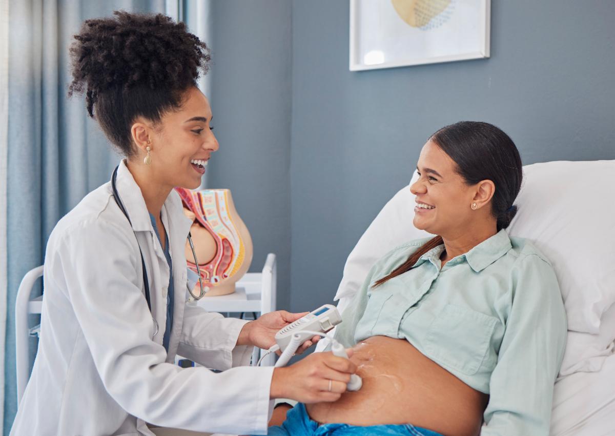 A pregnant patient smiles at her doctor while having her baby's heart rate checked.