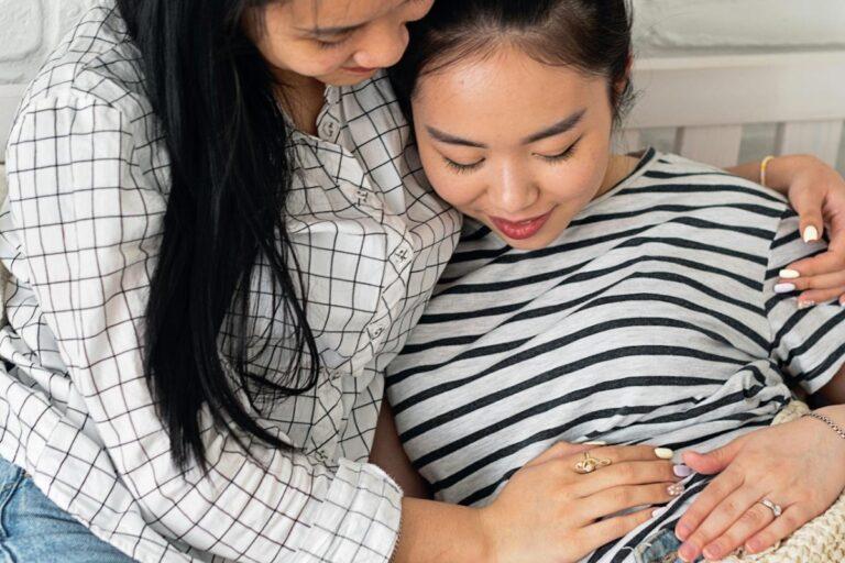 A young pregnant mother sits next to her mother as they both touch her stomach.