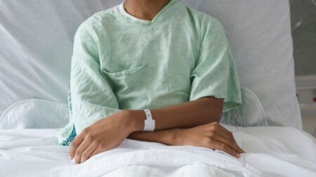 A teen patient sits in a hospital bed with arms crossed.