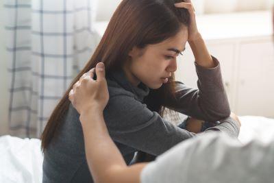 Depressed teen sitting with her head in her hand being comforted by a person sitting next to her.