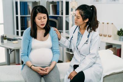 Distressed pregnant patient sits in doctor's office being comforted by her doctor sitting next to her.