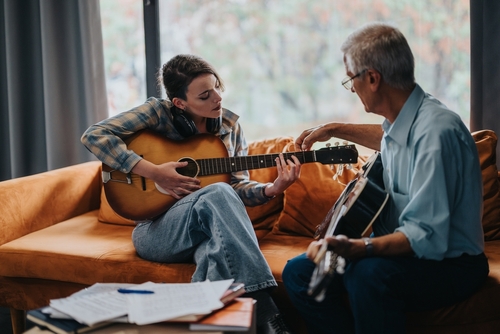 An experienced guitar teacher giving a lesson to a young student in a relaxed home setting_ highlighting musical education and learning.