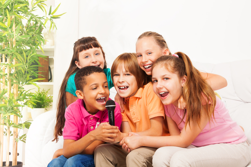 Close-up shoot of group of five happy little kids_ boys and girls_ singing together sitting on the coach in living room at home