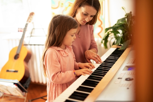 Woman and girl playing a piano. Beautiful mom teaching her daughter playing a piano.