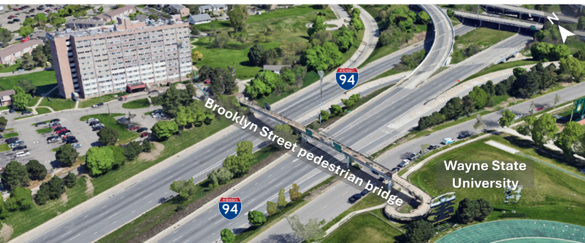 An aerial view of the Brooklyn Street pedestrian bridge over I-94, with the Trumbull Crossing apartments and Wayne State University on either side of the bridge.