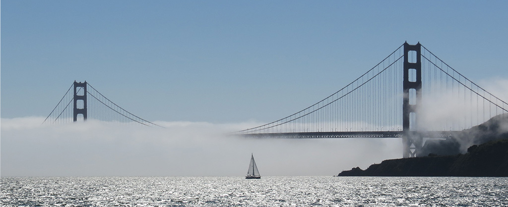 The Golden Gate Bridge shrouded in fog with a single sailboat sailing in front of it