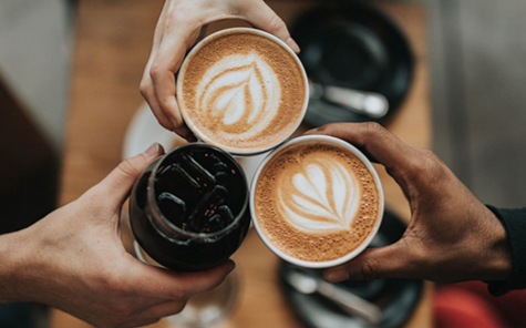 Hands of various shades of skin holding full cups of coffee with the open cups visible from above