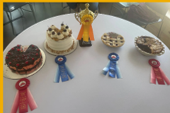 Cherry pies and cakes displayed on a table with prize ribbons in front.