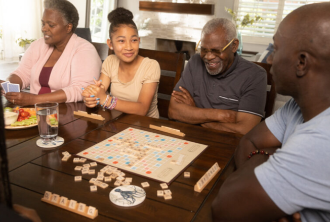 Black people of various ages sitting at a table with a scrabble game board