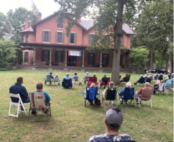 Shot of Rutherford B Hayes' house from a distance, with people sitting in lawn chairs on the front lawn in the foreground