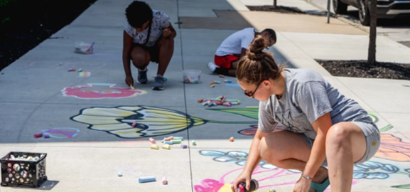 Young woman drawing on pavement with chalk, with two children in background