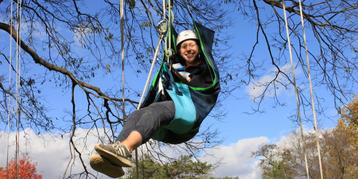 Person suspended from tree branch using adaptive equipment, demonstrating adaptive tree climbing