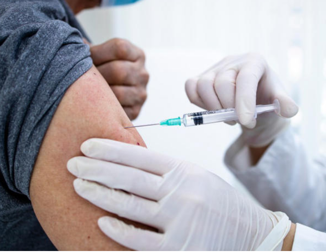 Hands in white latex gloves administering a vaccine into an arm with the sleeve listed
