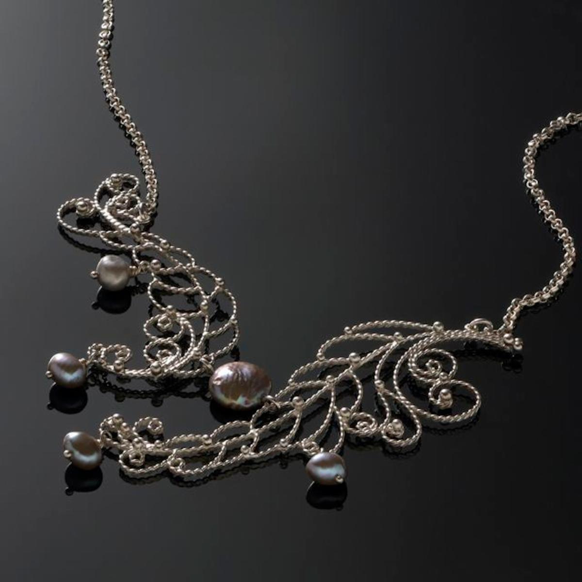 A photo of a silver necklace intricately shaped to look like feathers, with fresh water pearls.