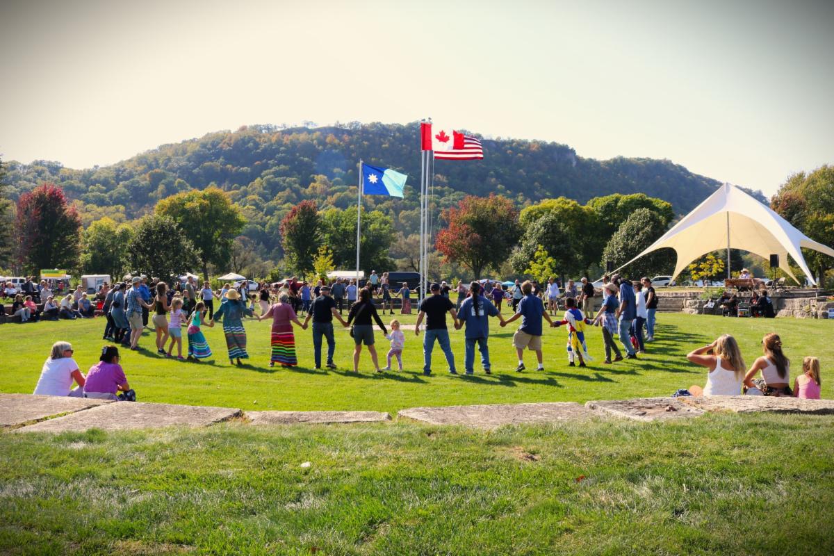 Photo of people holding hands in a circle with bluffs in the distance at Unity Park during a social round dance.