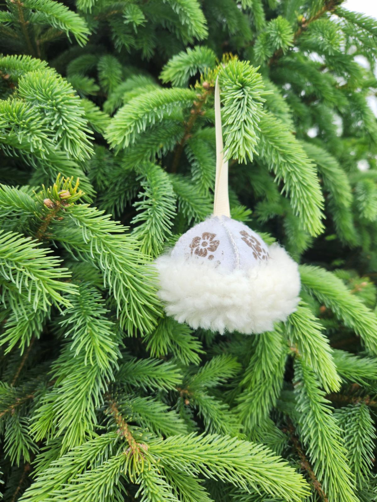 Sewn sheepskin white winter hat ornament hanging on an evergreen tree.
