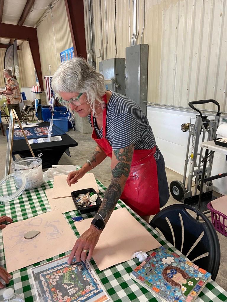 Mary Beth Magyar points to a picture of her mosaic design on a table in front of an unglazed clay tile.