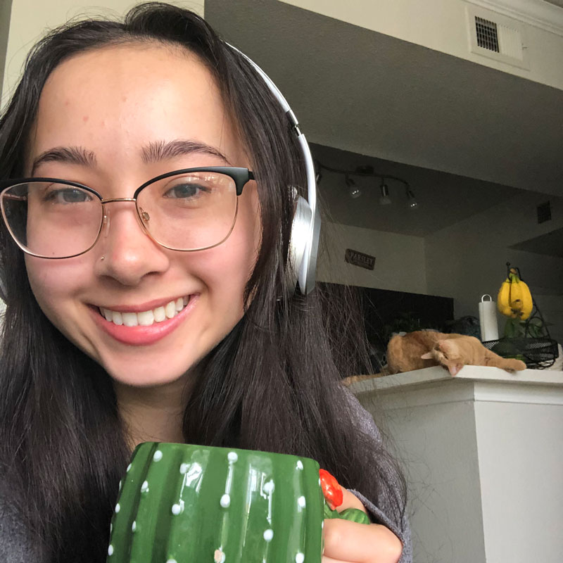 Marissa at home working remotely with cat in background coffee in hand and headphones on