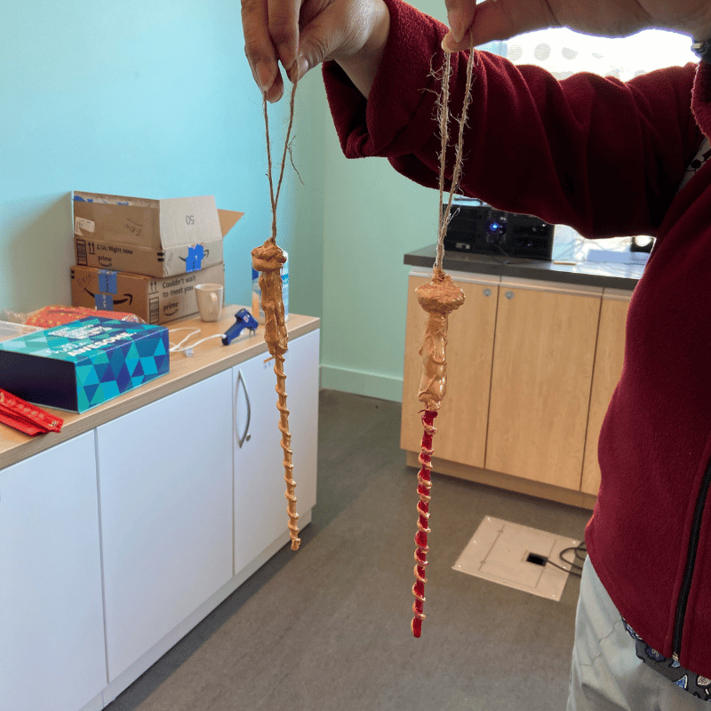 Person in a fuzzy red jacket and tan pans holds up two wants, with gold spindly handles and red/gold stems.