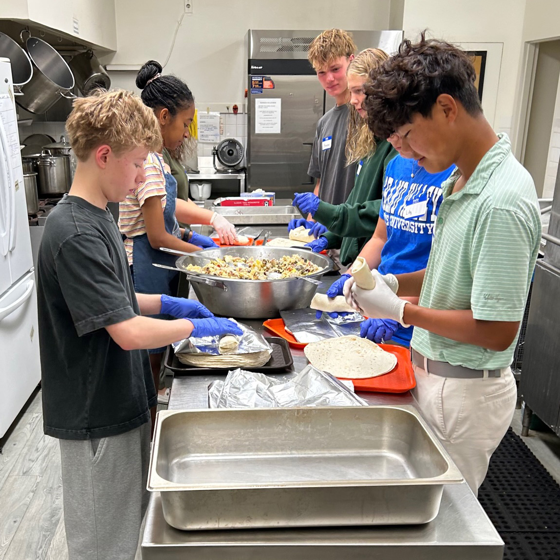 A group of teenagers assemble burritos