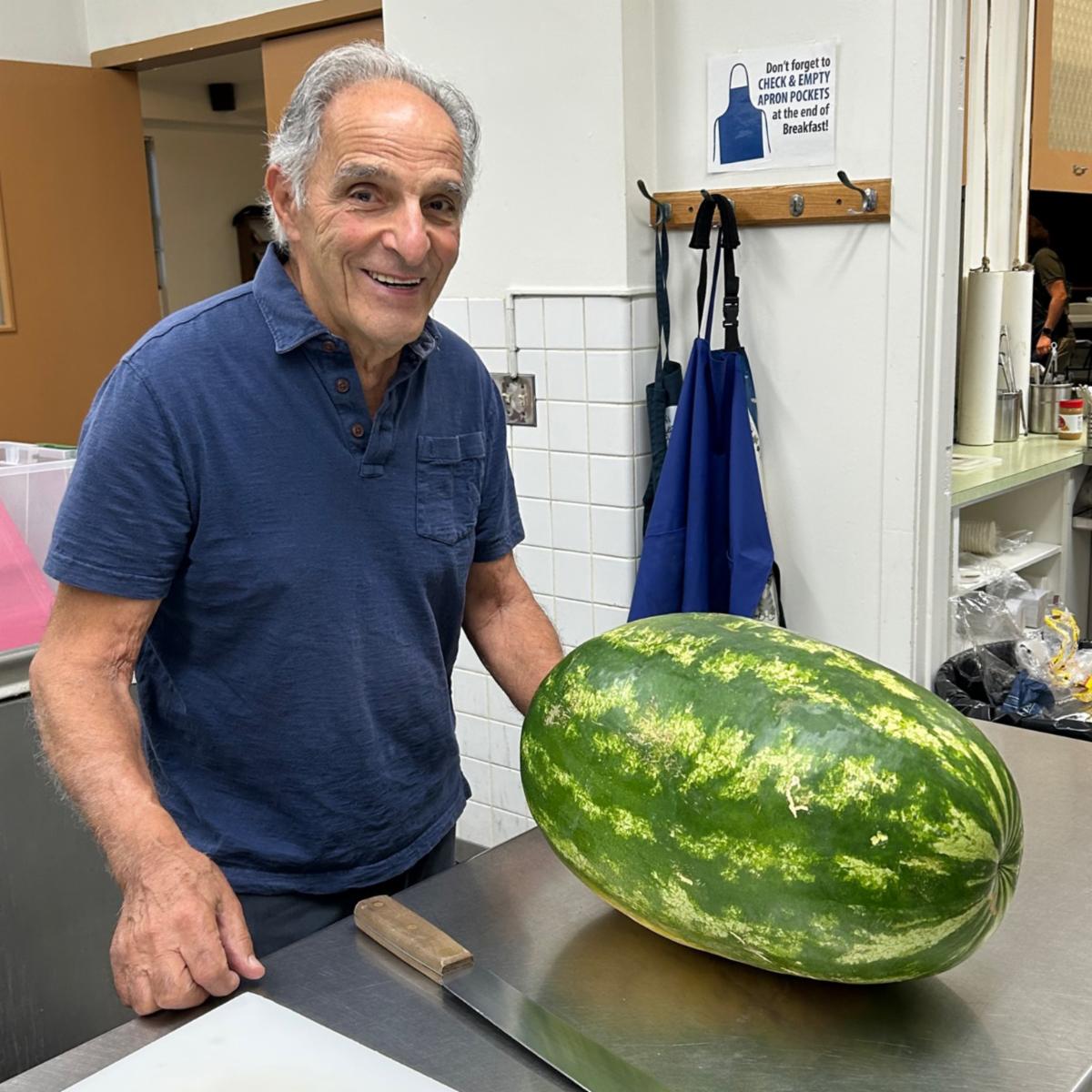 A man stands next to a large uncut watermelon