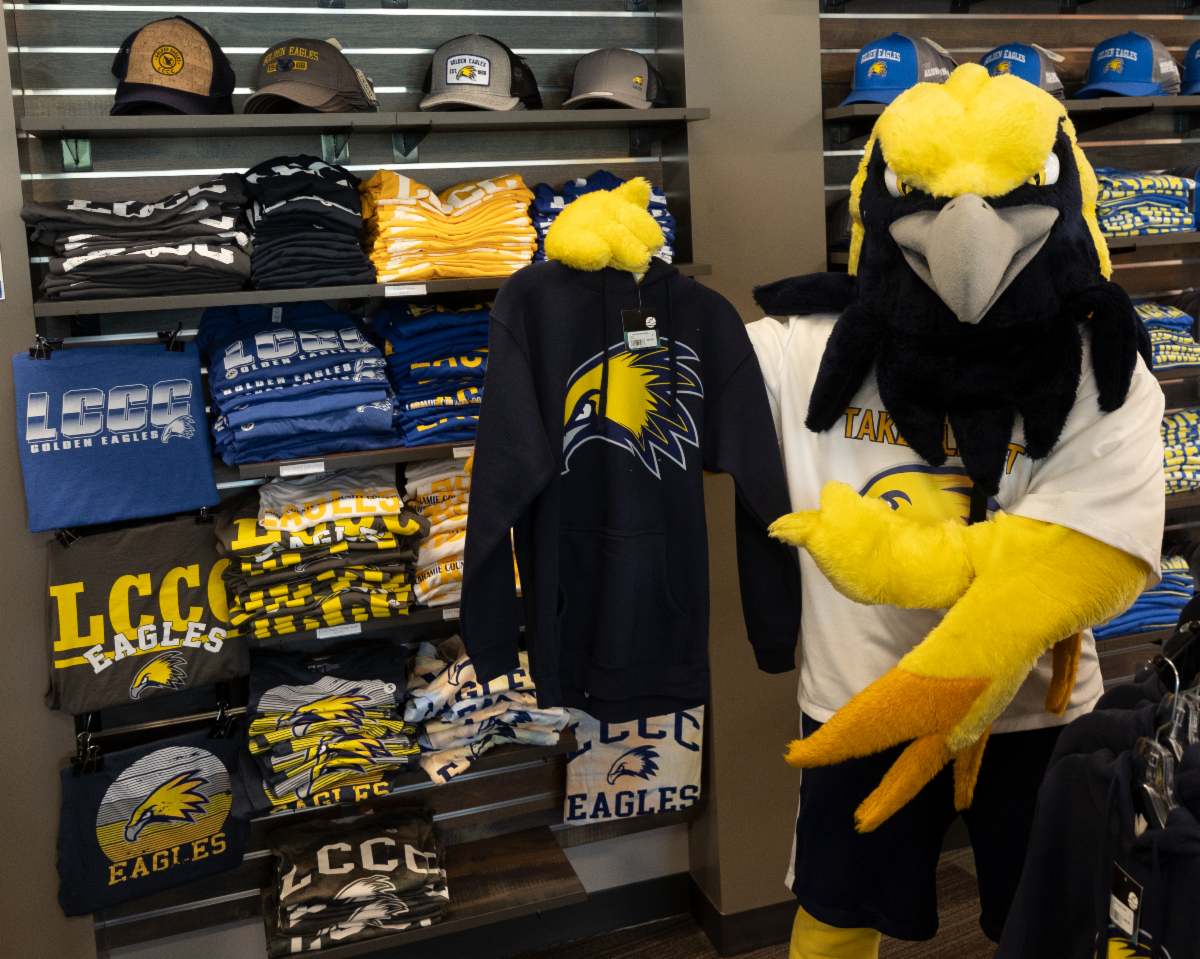 Talon stands in front of a colorful display wall of bookstore T-shirts, showcasing LCCC merchandise.