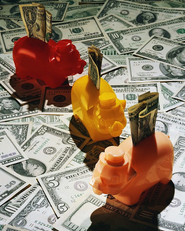 Photo of three piggy banks on a background of US currency bills