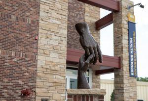 Two hands holding a statue, positioned in front of the Health Science Building on the Cheyenne campus.