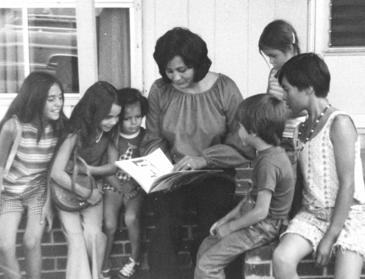 Betty Benavidez reading a book while surrounded by six students