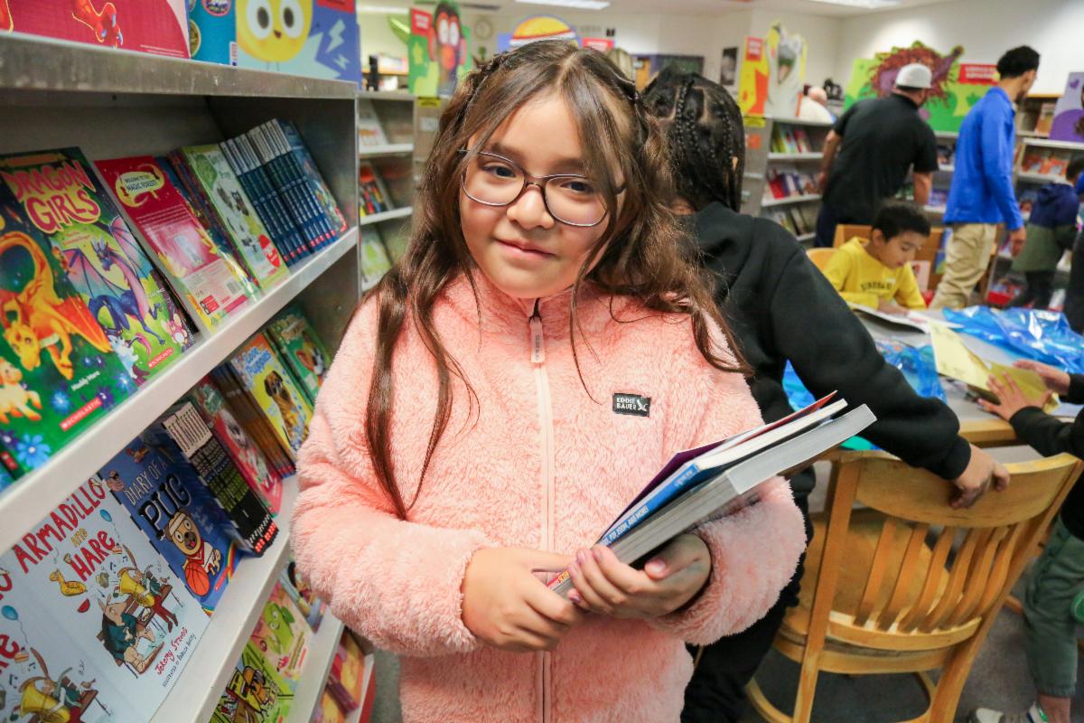 A student in a library holding some books.